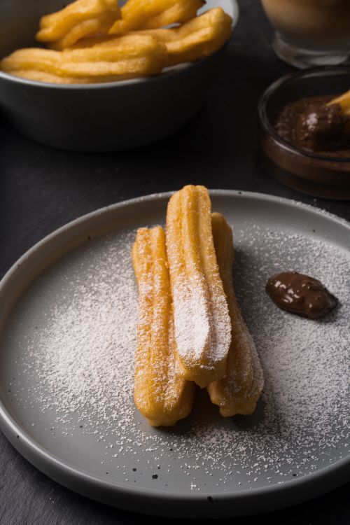 Free Delicious churros dusted with powdered sugar served on a plate with rich chocolate sauce. Stock Photo