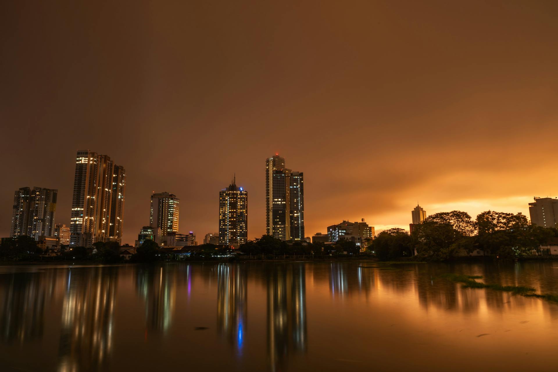 Dramatic twilight skyline of Colombo, Sri Lanka with city lights reflected on calm lake waters.