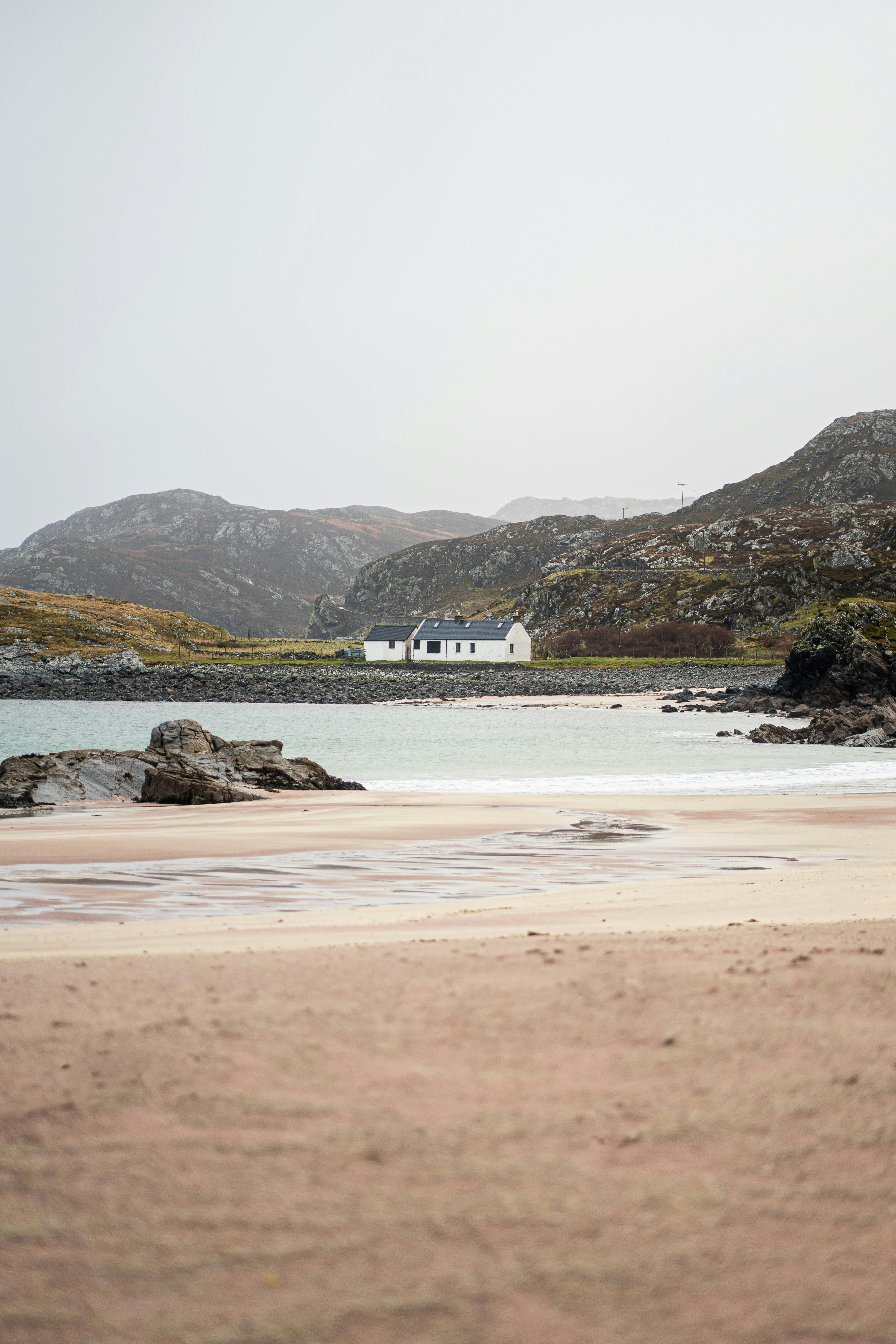 Tranquil remote cottage by the coast, nestled between rugged hills and sandy beach.