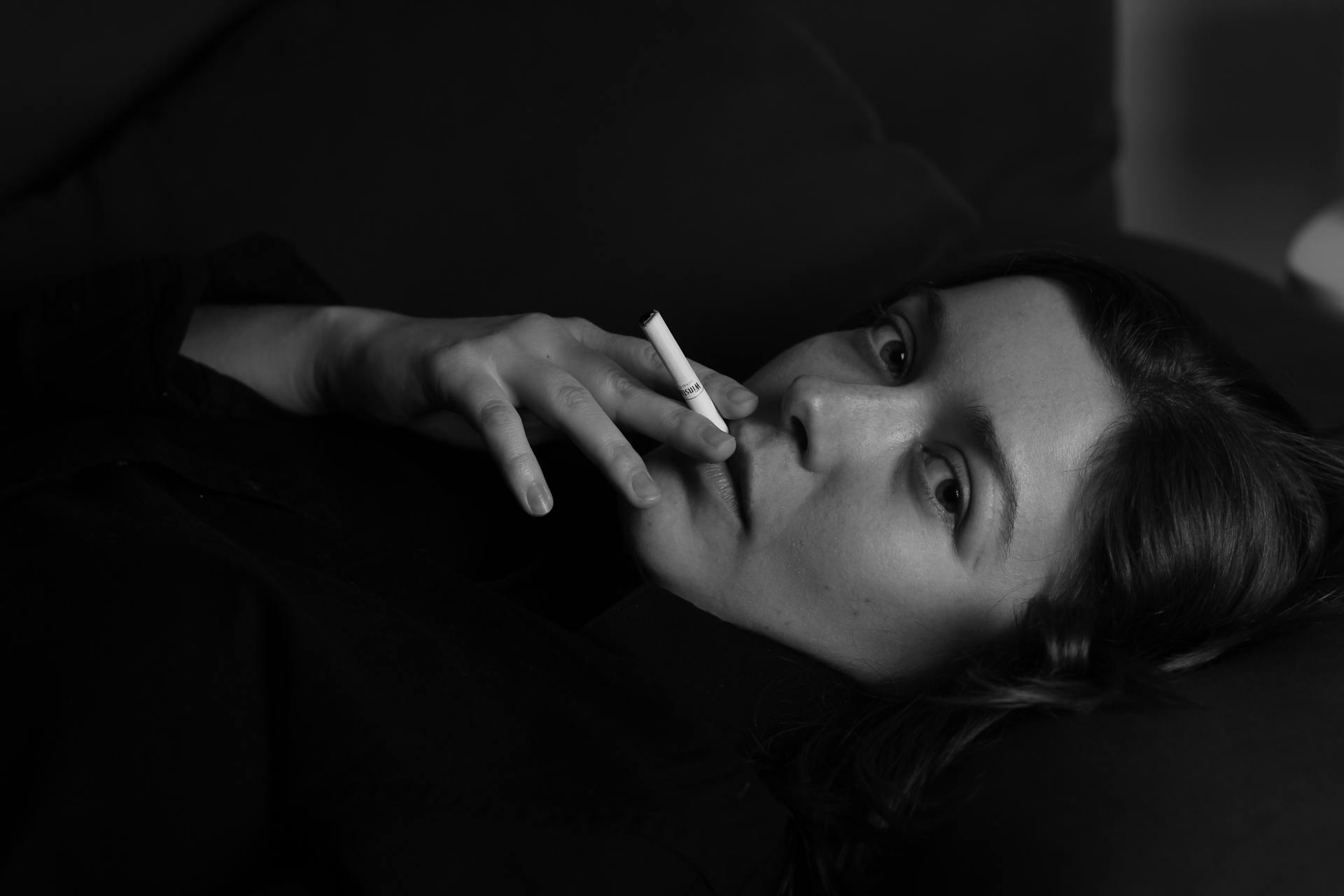 Black and white portrait of a young woman smoking indoors, embodying a moody and edgy style.