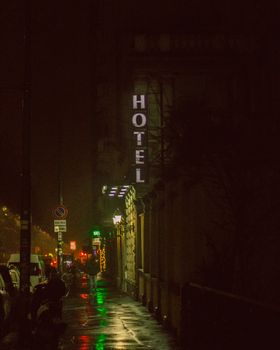 Atmospheric nighttime street scene with a glowing neon hotel sign reflecting on wet pavement.