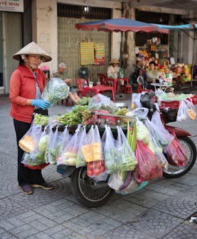 A street vendor in Vietnam selling fresh vegetables from a scooter in a busy market setting.