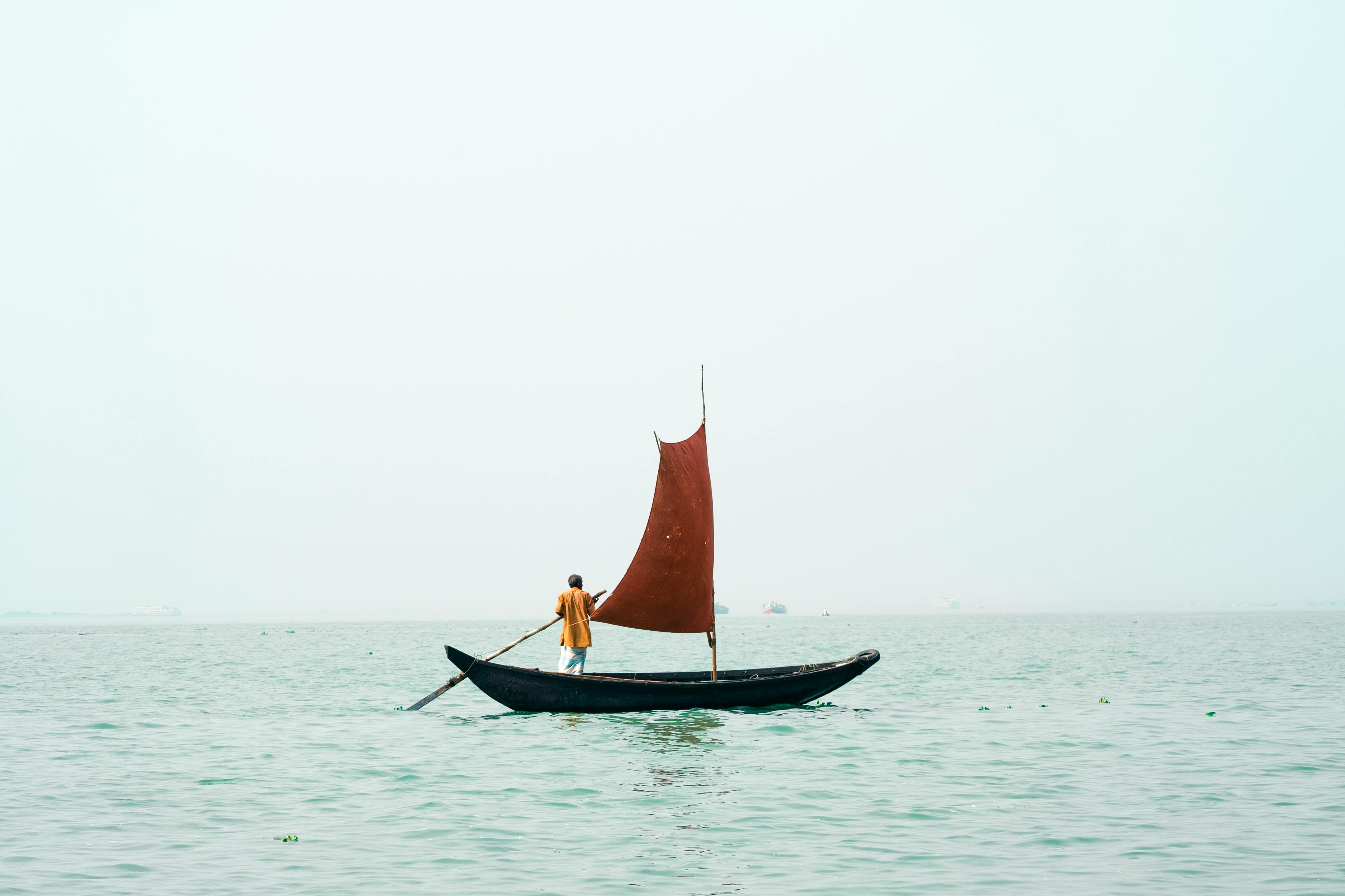 a man rowing a small boat with a sail