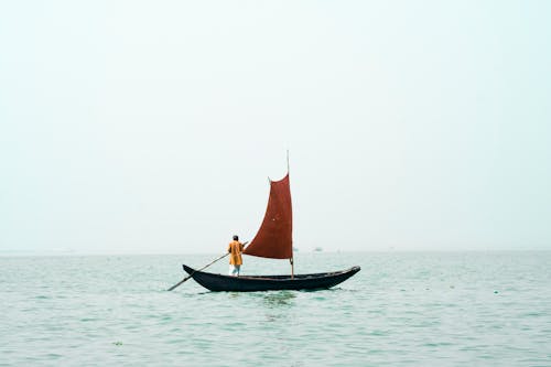 Мужчина гребет на маленькой лодке с парусом