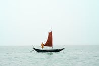 A Man Rowing A Small Boat With a Sail