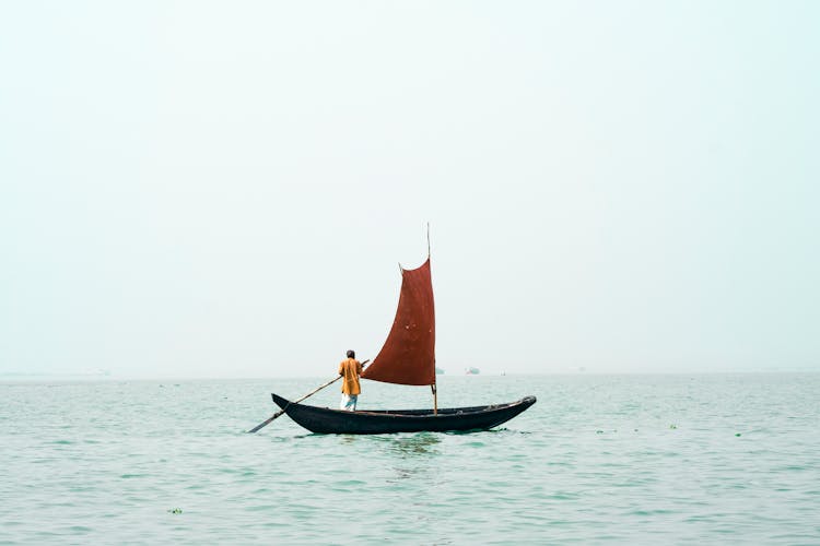 A Man Rowing A Small Boat With A Sail