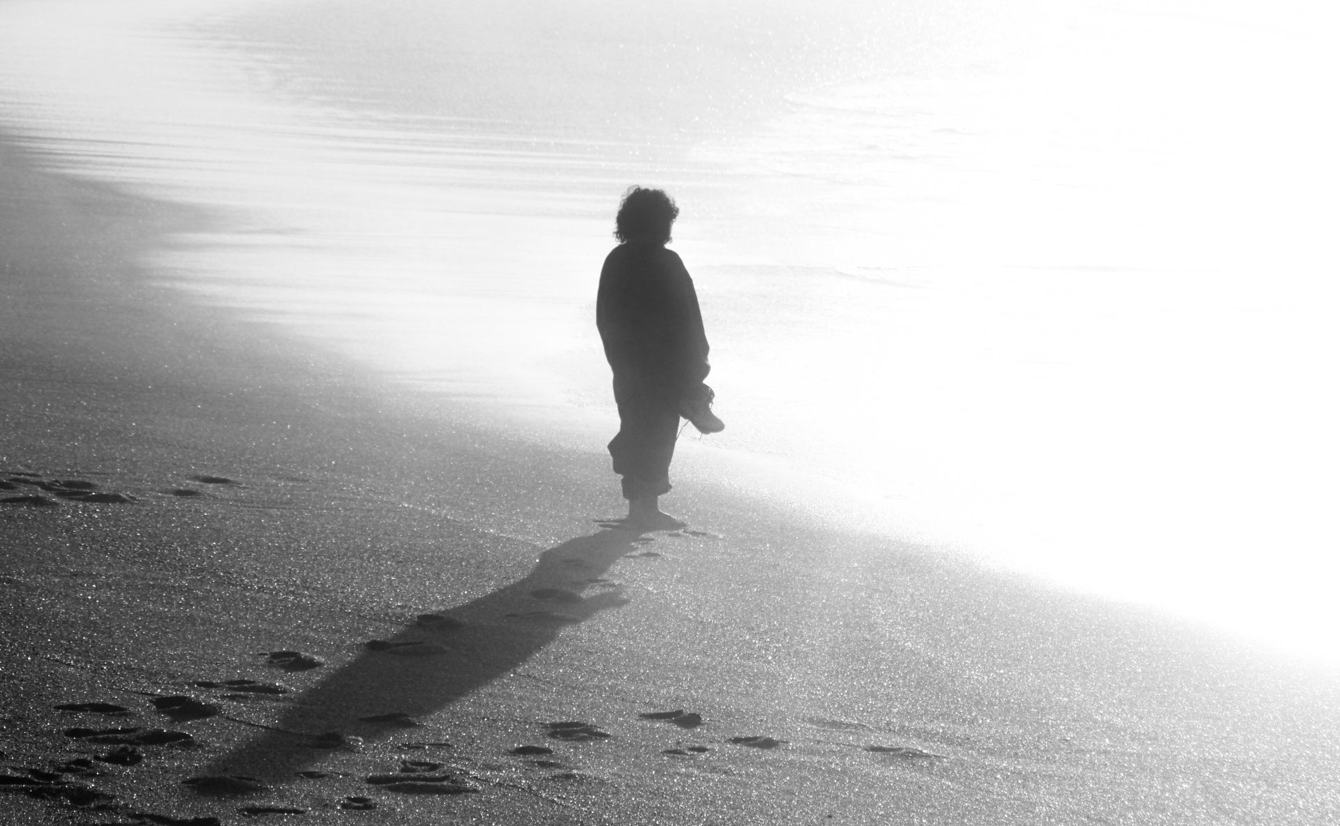 A solitary figure casts a long shadow on a tranquil beach in Rabat, Morocco, during a calm day.