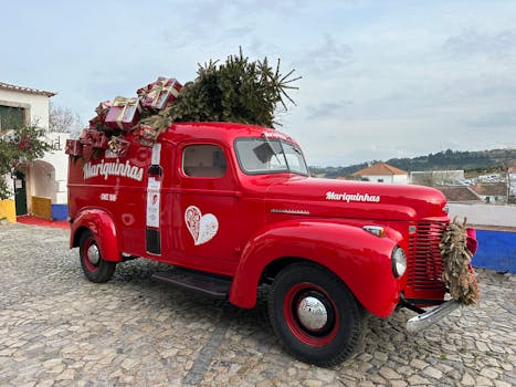 A festive vintage red truck adorned with Christmas gifts and a tree, parked in Óbidos, Portugal.