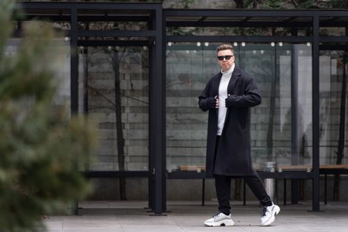 Free Fashionable man in sunglasses and long coat standing confidently in urban setting. Stock Photo