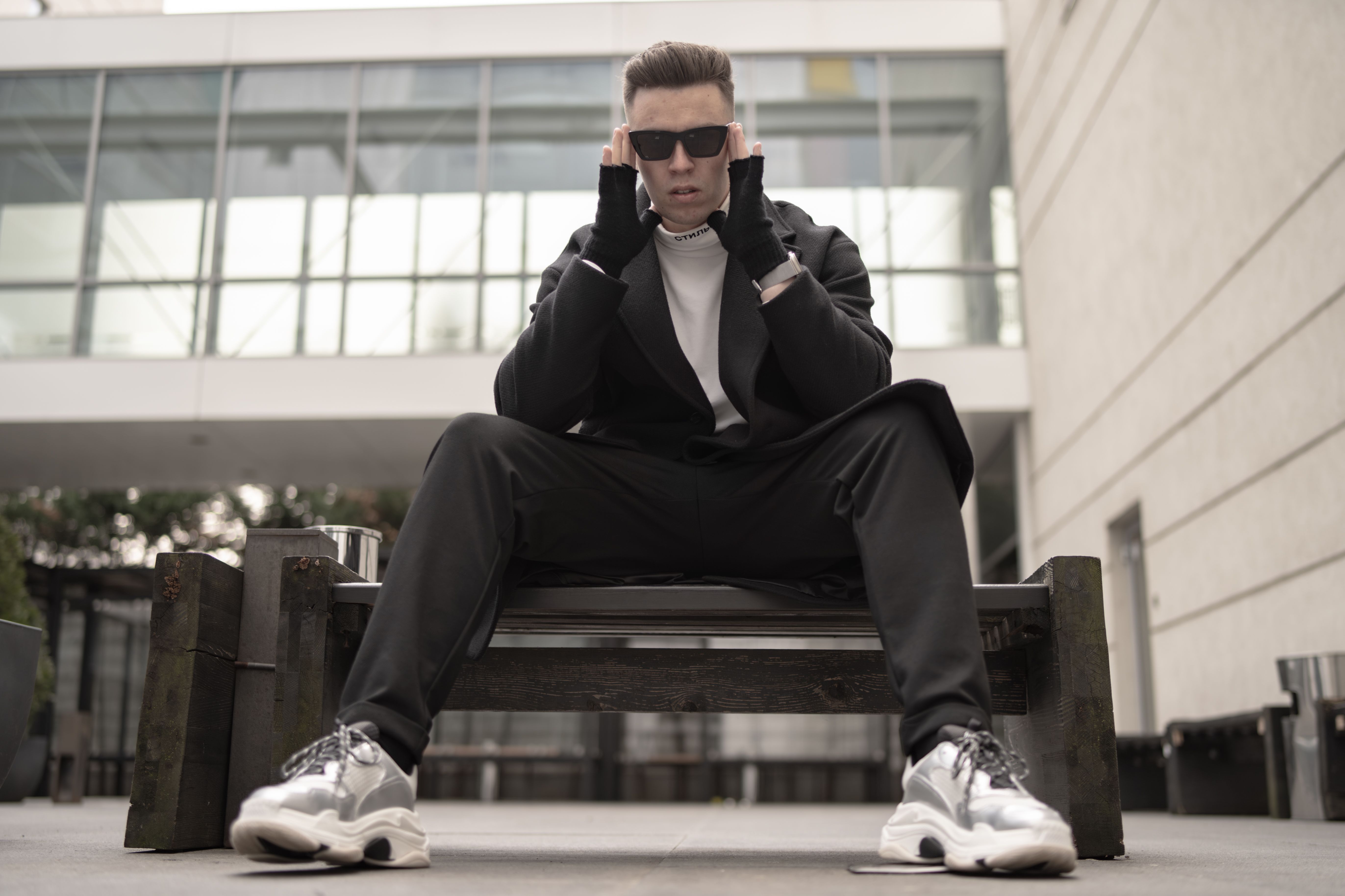 Homme assis en tenue streetwear noire complète dans un environnement urbain moderne