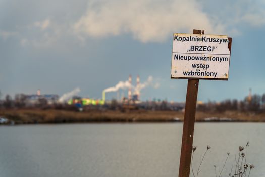 Sign at Brzegi gravel pit with industrial backdrop, no entry for unauthorized access.