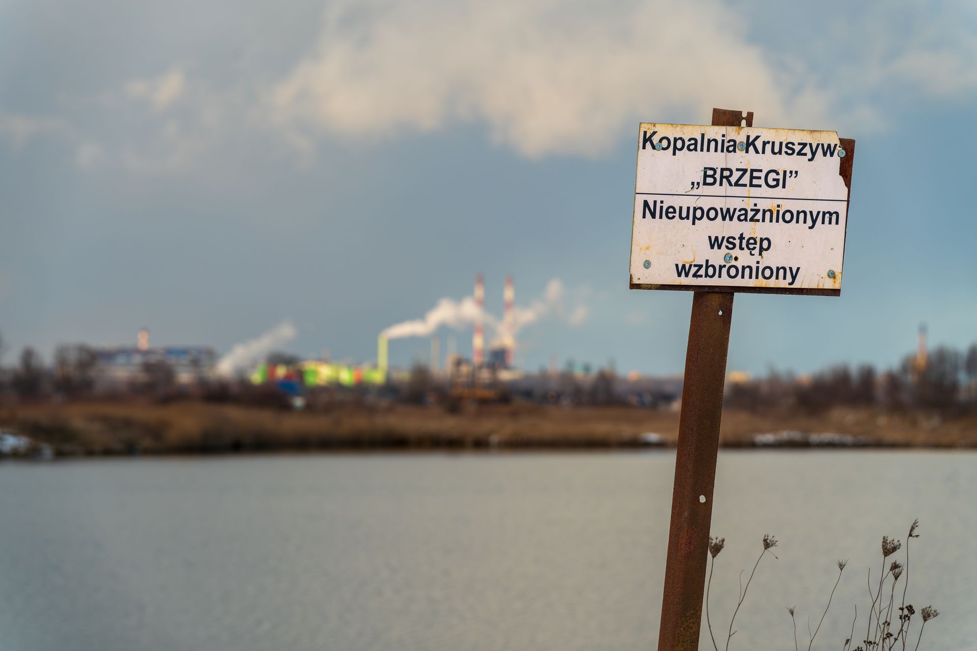 Sign at Brzegi gravel pit with industrial backdrop, no entry for unauthorized access.
