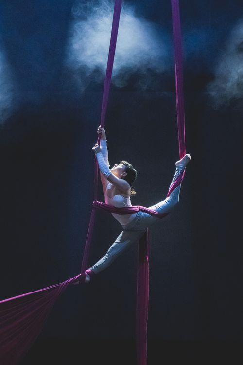 Free A stunning aerial acrobat performing gracefully on silks with dramatic lighting and smoke effects. Stock Photo