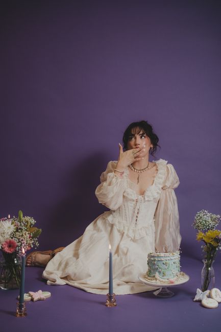 A woman in a vintage dress celebrates with a decorative cake and flowers.
