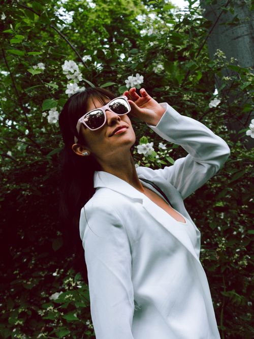 Free Elegant woman in white blazer and sunglasses posing amidst lush greenery in Madrid. Stock Photo