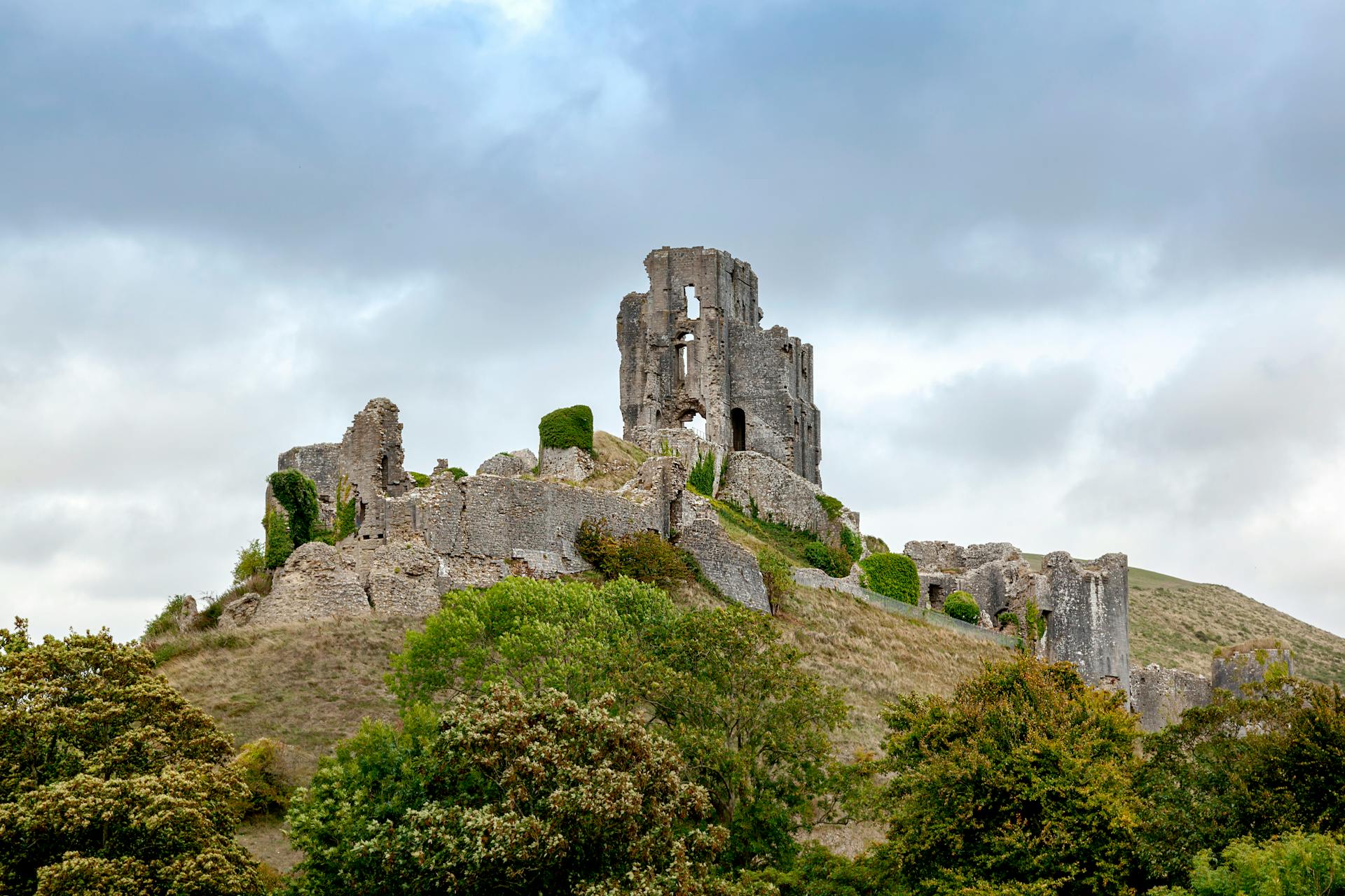 Explore the ancient ruins of Corfe Castle on a cloudy day in Dorset, England.