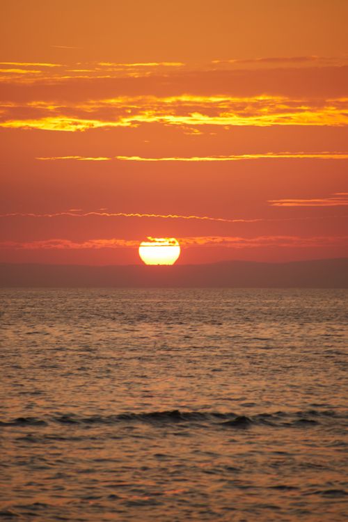 Free Scenic ocean view with a vibrant sunset over calm waters and colorful sky. Stock Photo