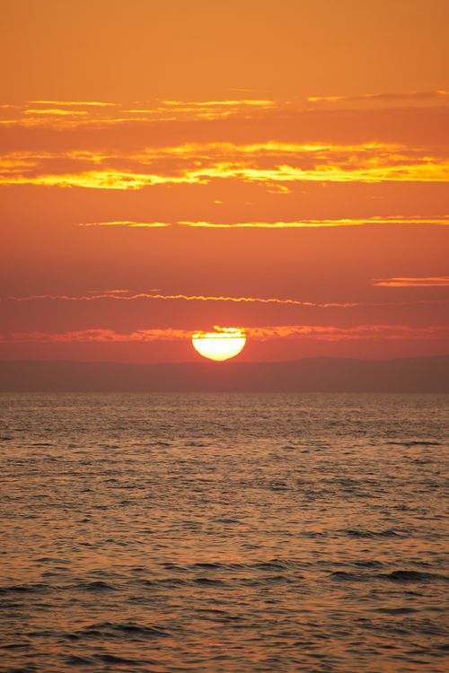 Free Breathtaking view of the sun setting over the ocean, casting vibrant colors across the sky. Stock Photo