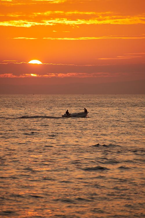Free Stunning sunset over the ocean with a silhouetted boat for tranquil ambiance. Stock Photo