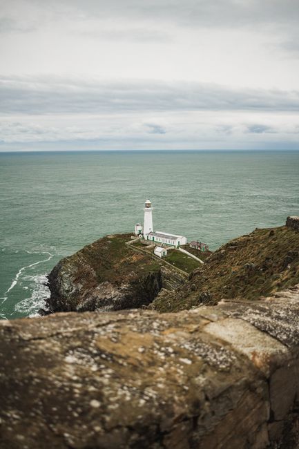 A solitary lighthouse stands on a rugged cliff, overlooking the vast ocean, against a cloudy sky.