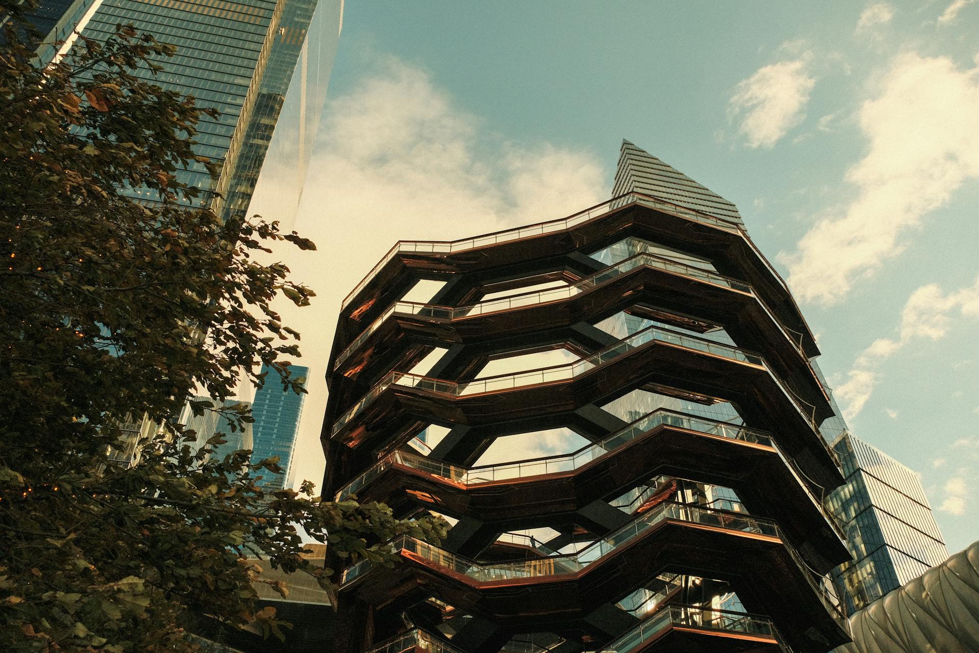 Unique architectural view of the Vessel in New York surrounded by skyscrapers and trees.
