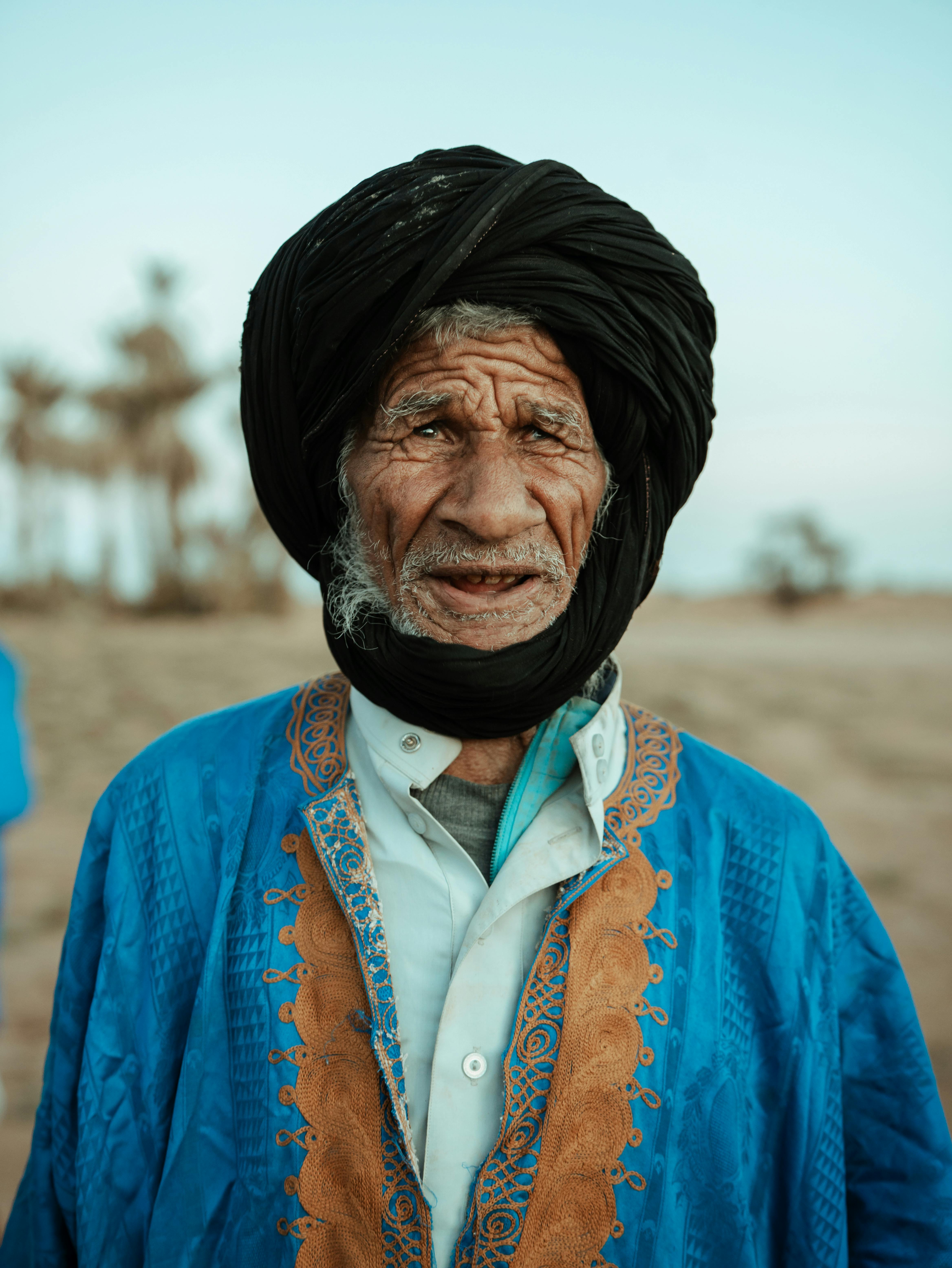 A striking portrait of an elderly nomadic man in traditional attire in the Mhamid desert, Morocco.