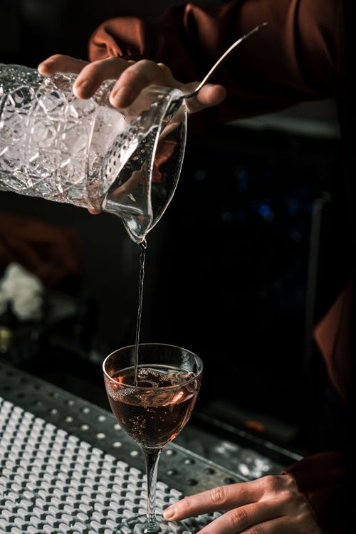 Free Bartender expertly pouring a cocktail into a glass, creating a moody and sophisticated bar scene. Stock Photo