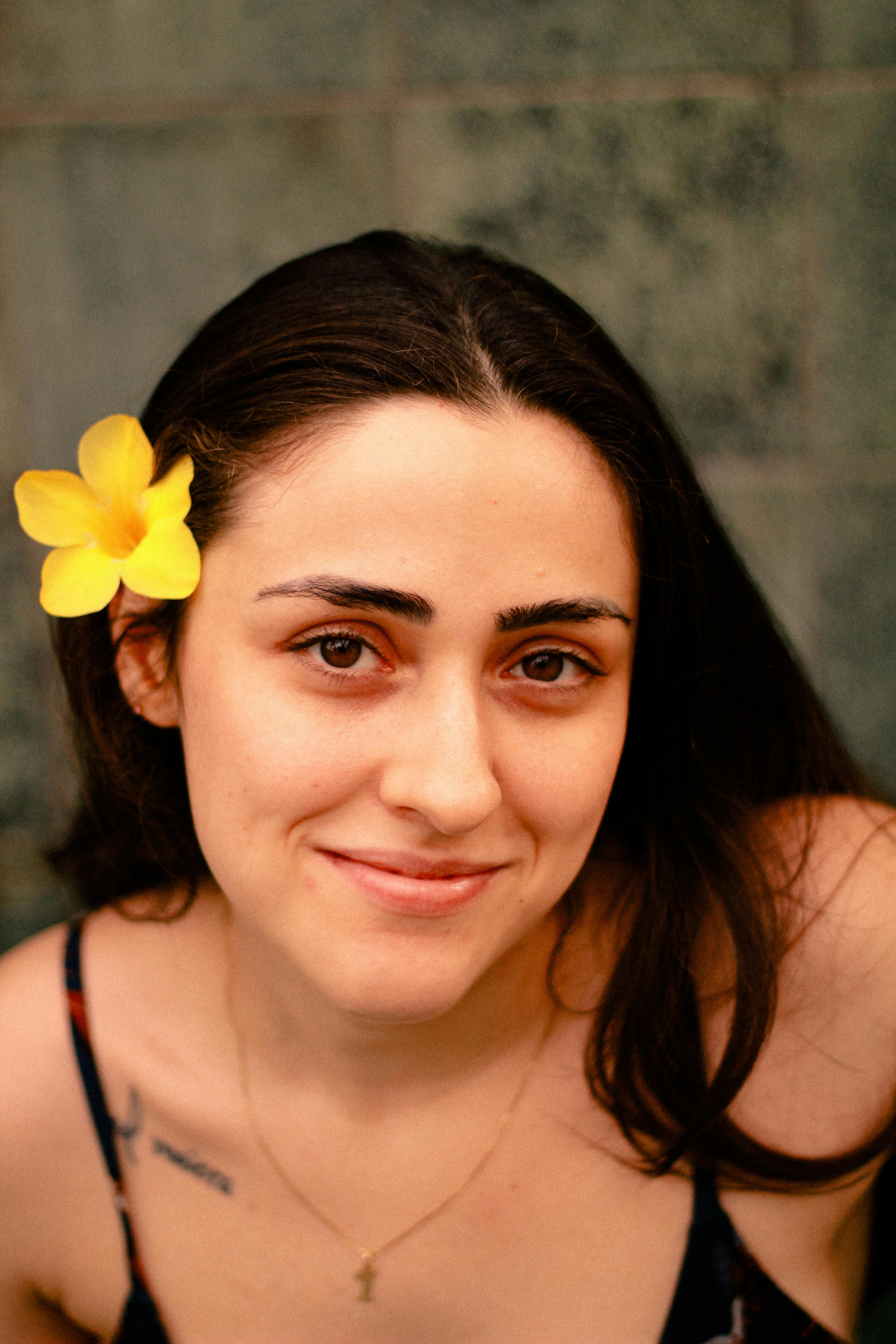 Close-up portrait of a smiling woman with a yellow flower behind her ear.