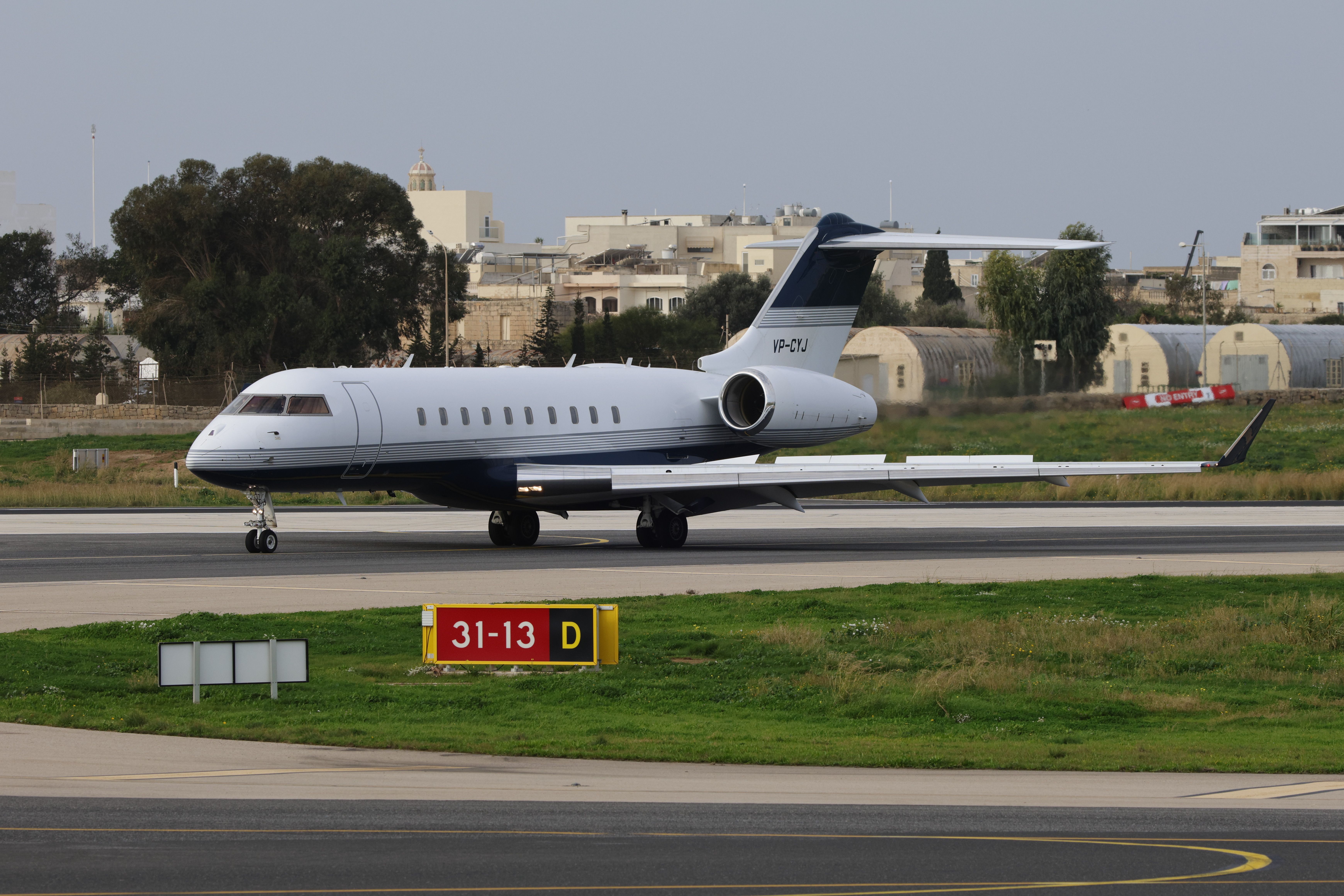 A sleek private jet parked on a runway with urban buildings in the background.