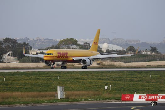 DHL cargo plane taxiing on a runway at an airport on a clear day with cityscape background.
