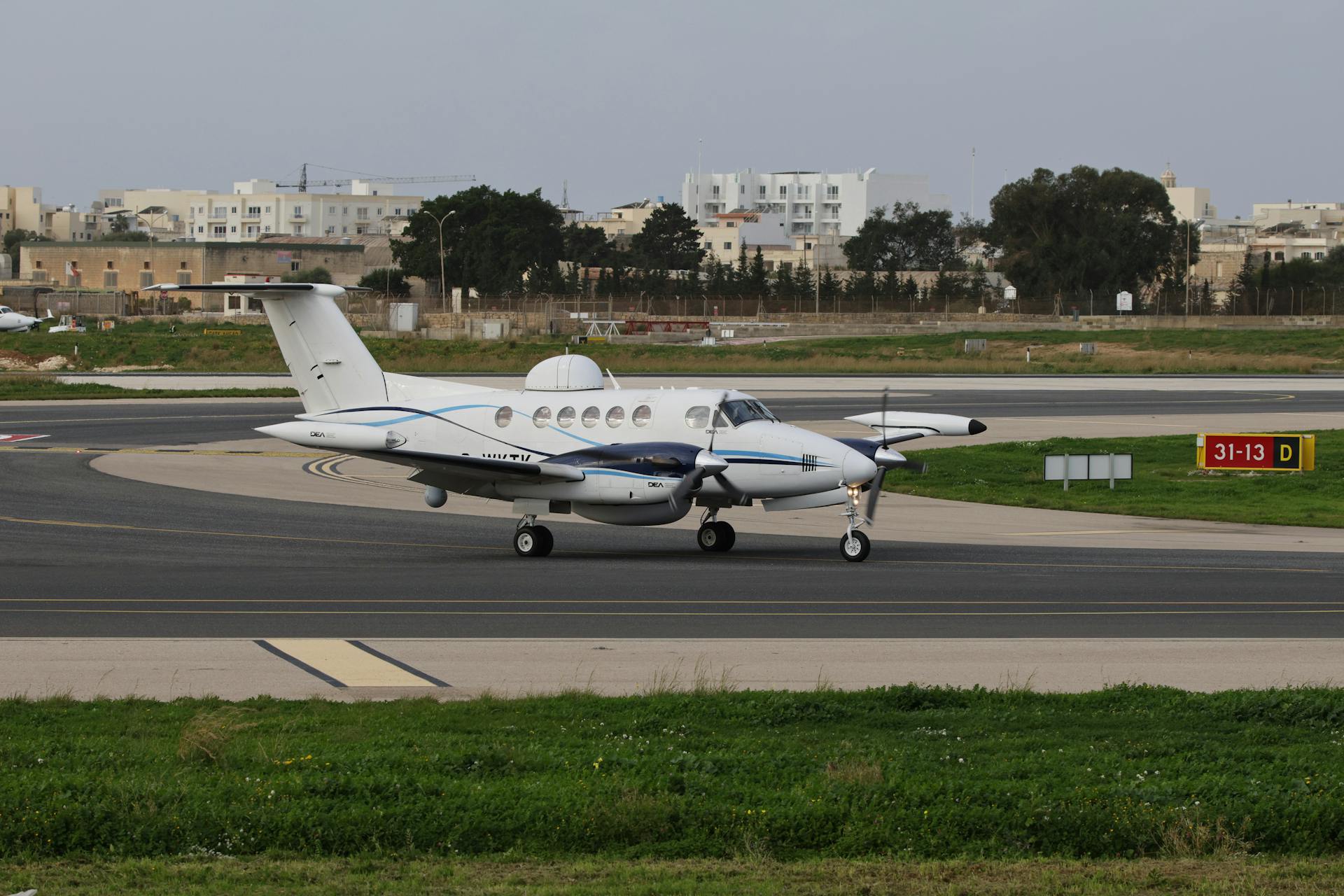 A private aircraft parked on the runway with urban buildings in the background.