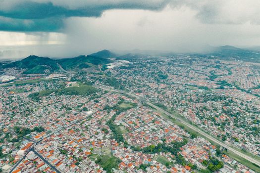 A wide aerial shot of a city landscape with an incoming storm, showing urban sprawl and green hills.