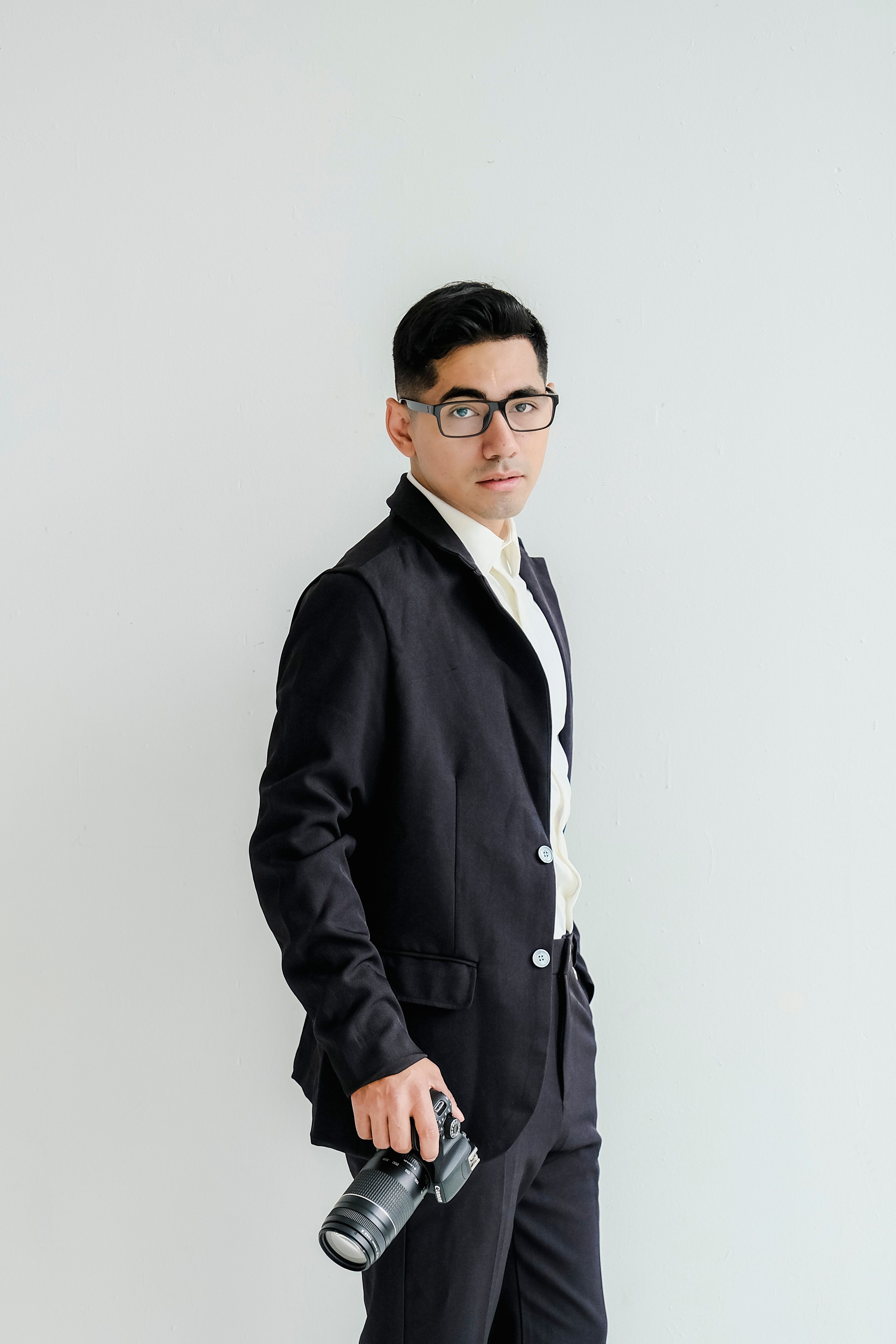 A man in formal attire holding a camera in a bright studio setting.