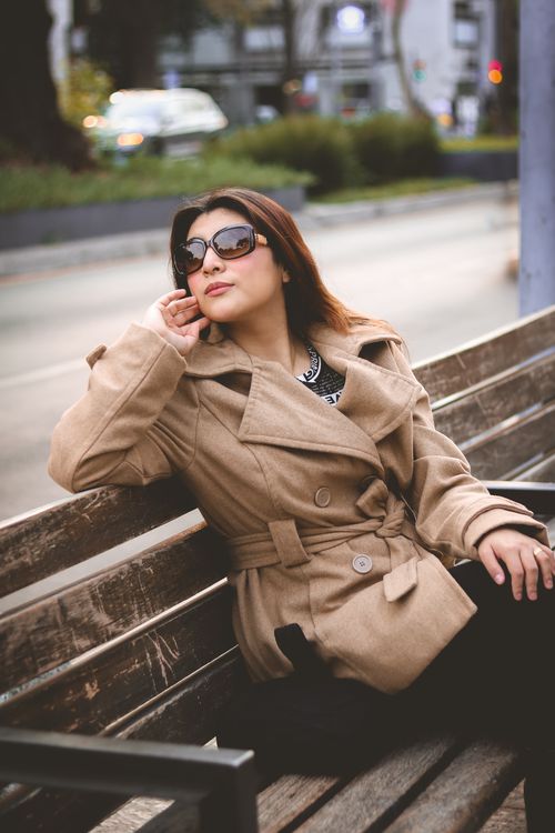 Free A fashionable woman wearing sunglasses enjoys a relaxing moment on a park bench during autumn. Stock Photo