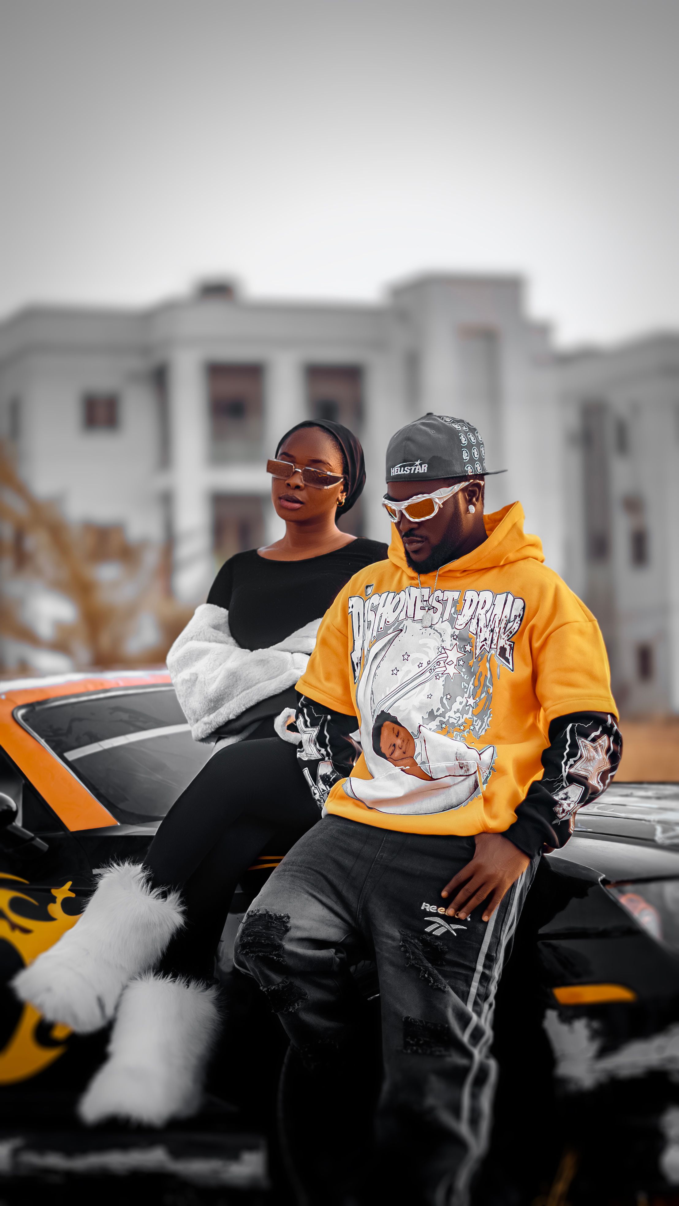 Stylish couple posing with a sports car in urban setting.
