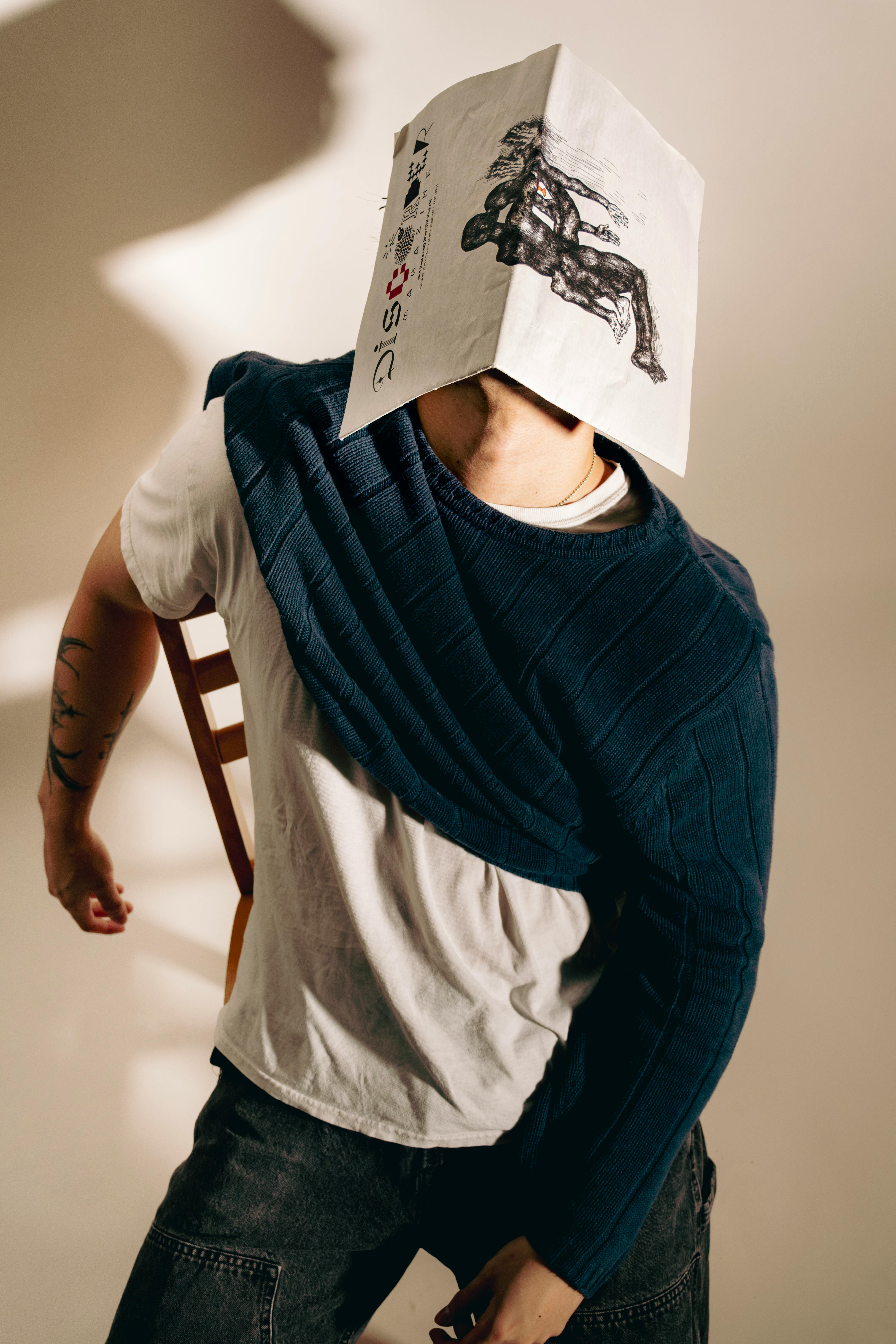 Creative studio portrait of a man with a newspaper mask, showcasing tattoos and artistic lighting.