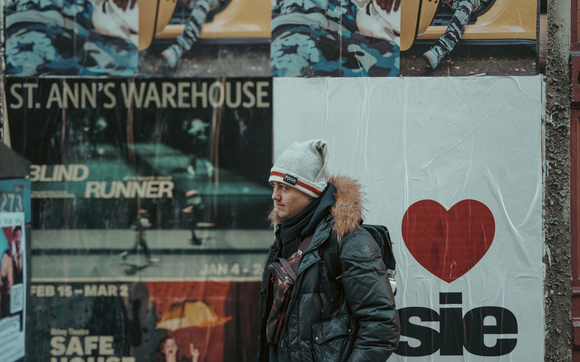 A person in winter clothing walks past posters on a street in New York City.