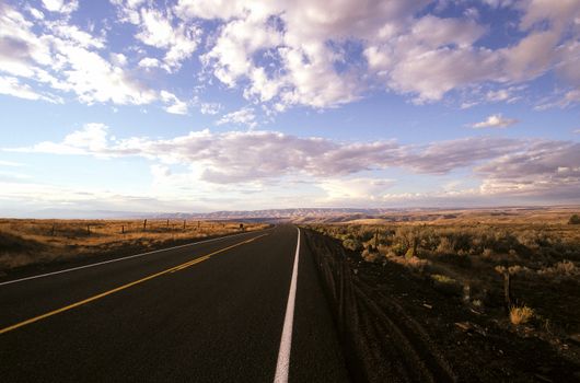A tranquil, endless road stretches through Oregon's vast landscape under a dramatic sky.