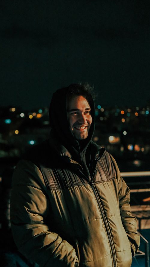 Free A joyful young man in a winter coat smiling in the city lights of İstanbul at night. Stock Photo