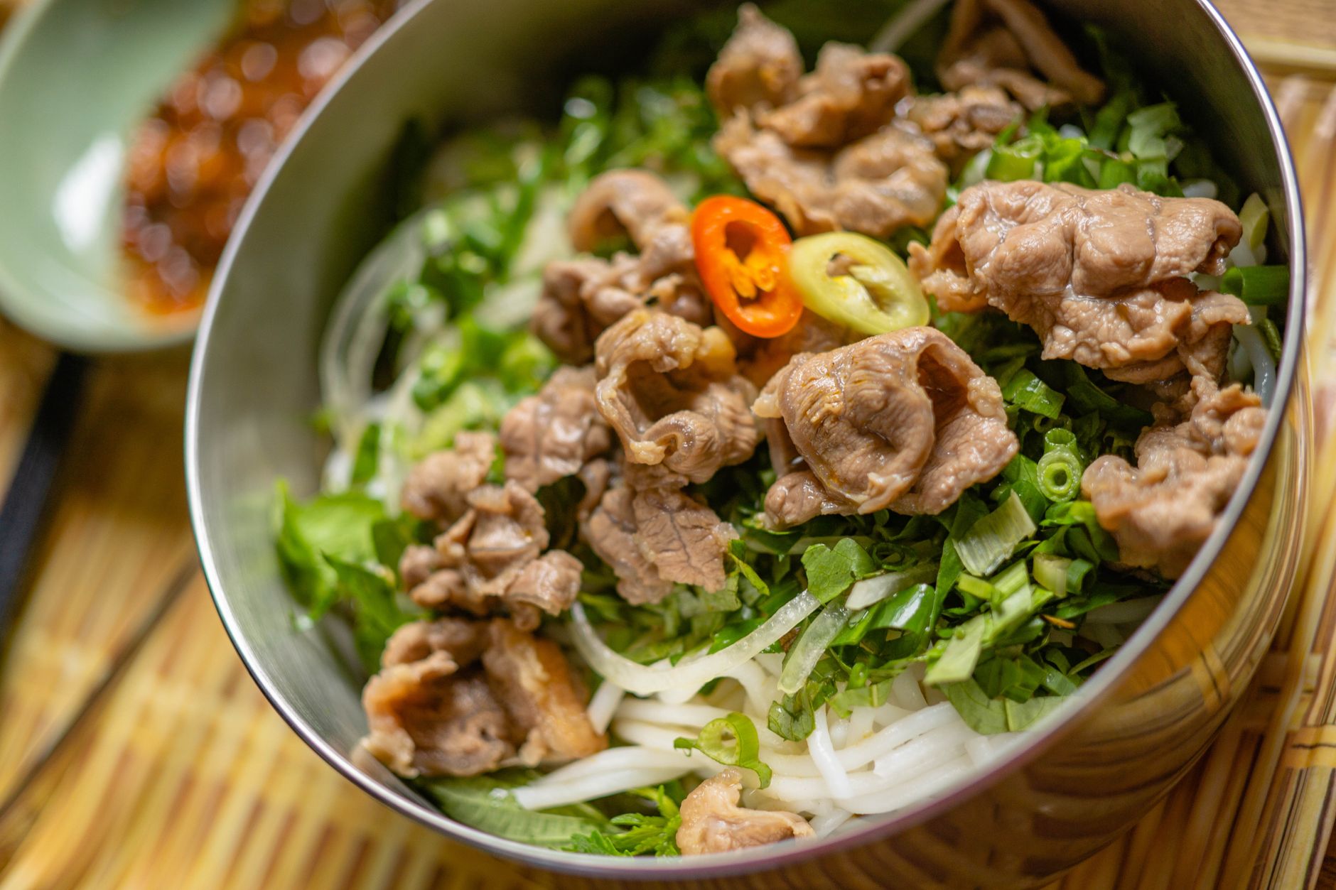 A tantalizing bowl of Vietnamese beef noodles with fresh herbs and chili peppers.