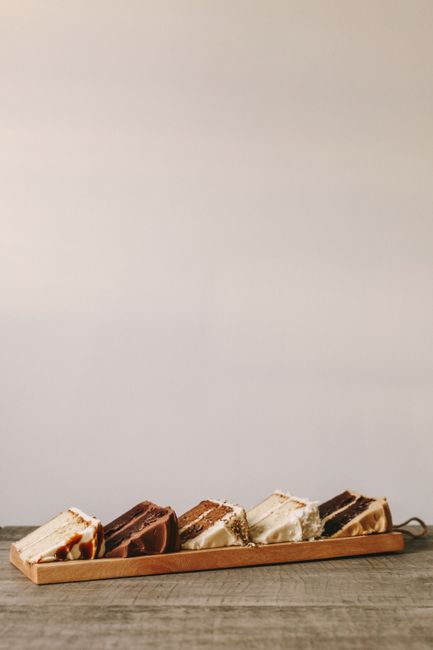 Five artisan cake slices presented on a wooden tray with minimalist style.