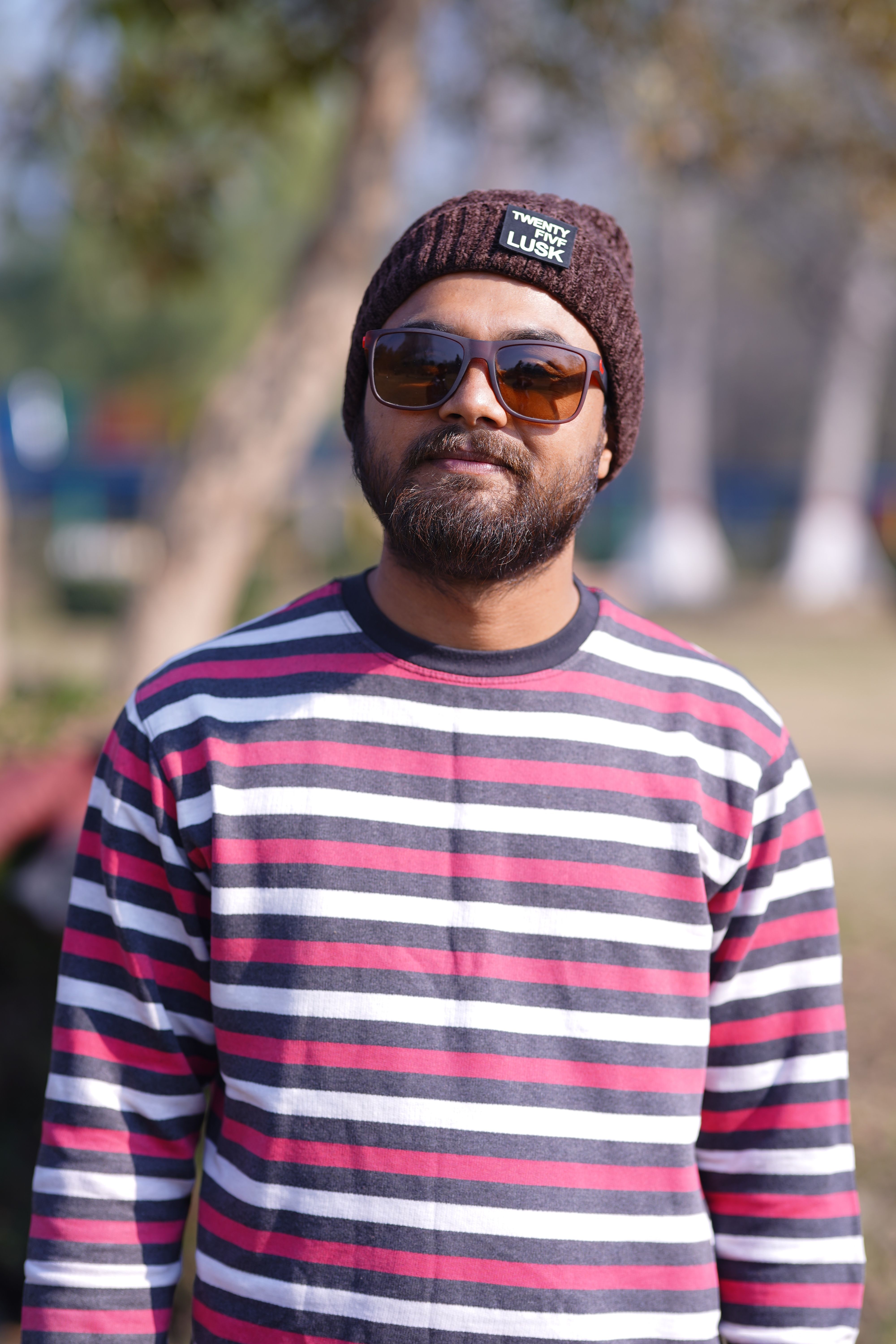 A casual portrait of a man wearing a striped sweater and sunglasses outdoors.