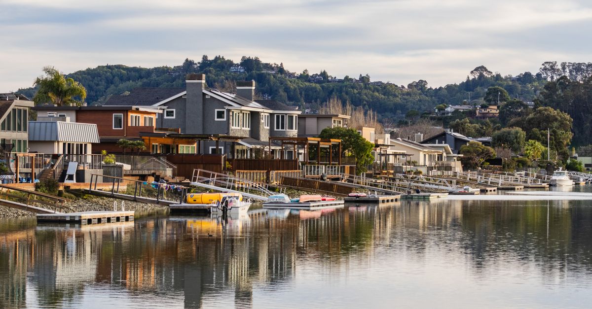 Charming waterfront houses with boats along a serene waterway and hillside background.