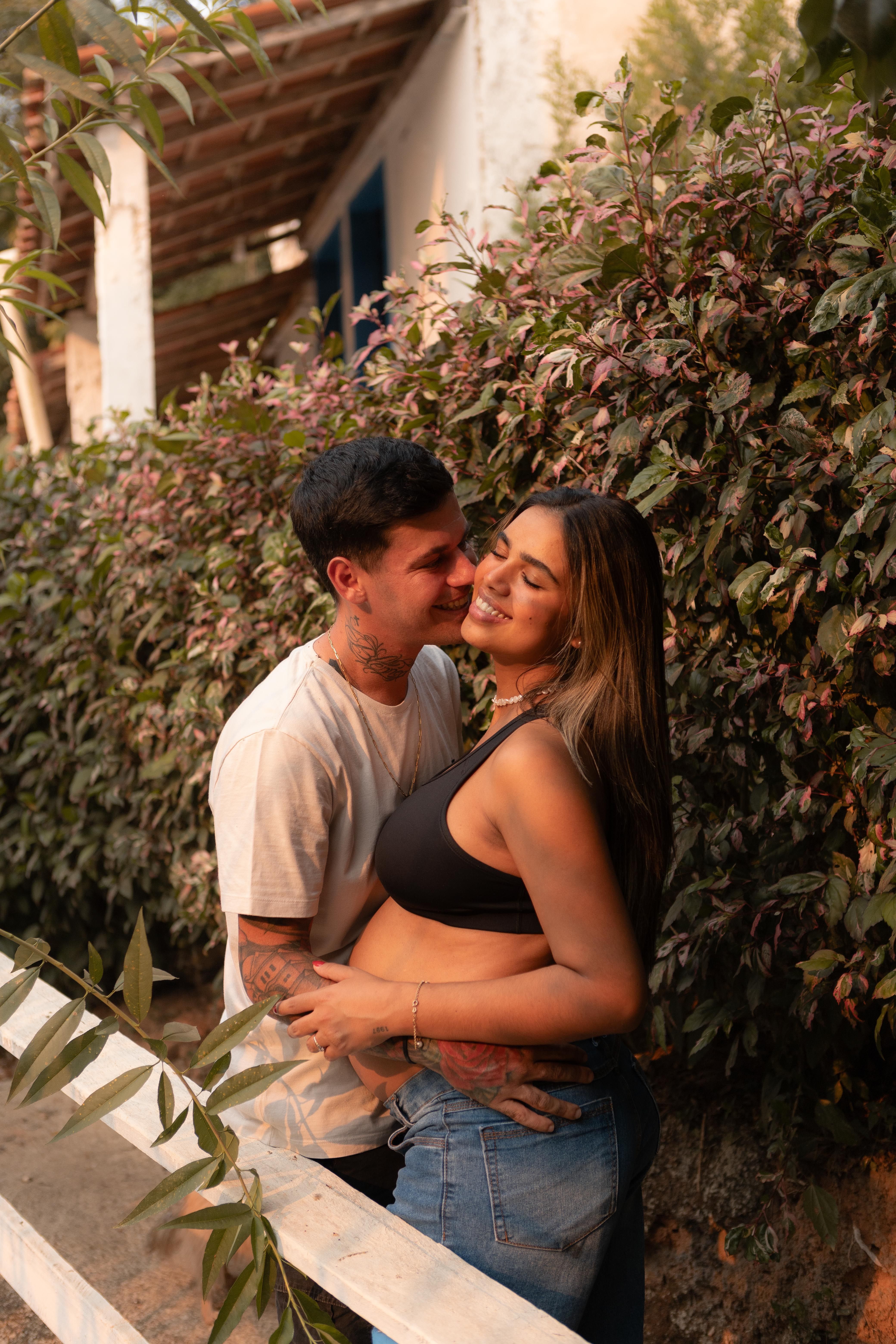 Couple in a loving embrace by a rustic fence with lush foliage.