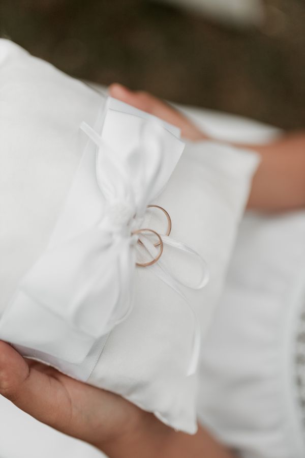 Gold wedding rings on a white satin pillow with ribbon