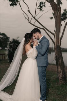 Bride and groom embrace during outdoor wedding ceremony by a lake.