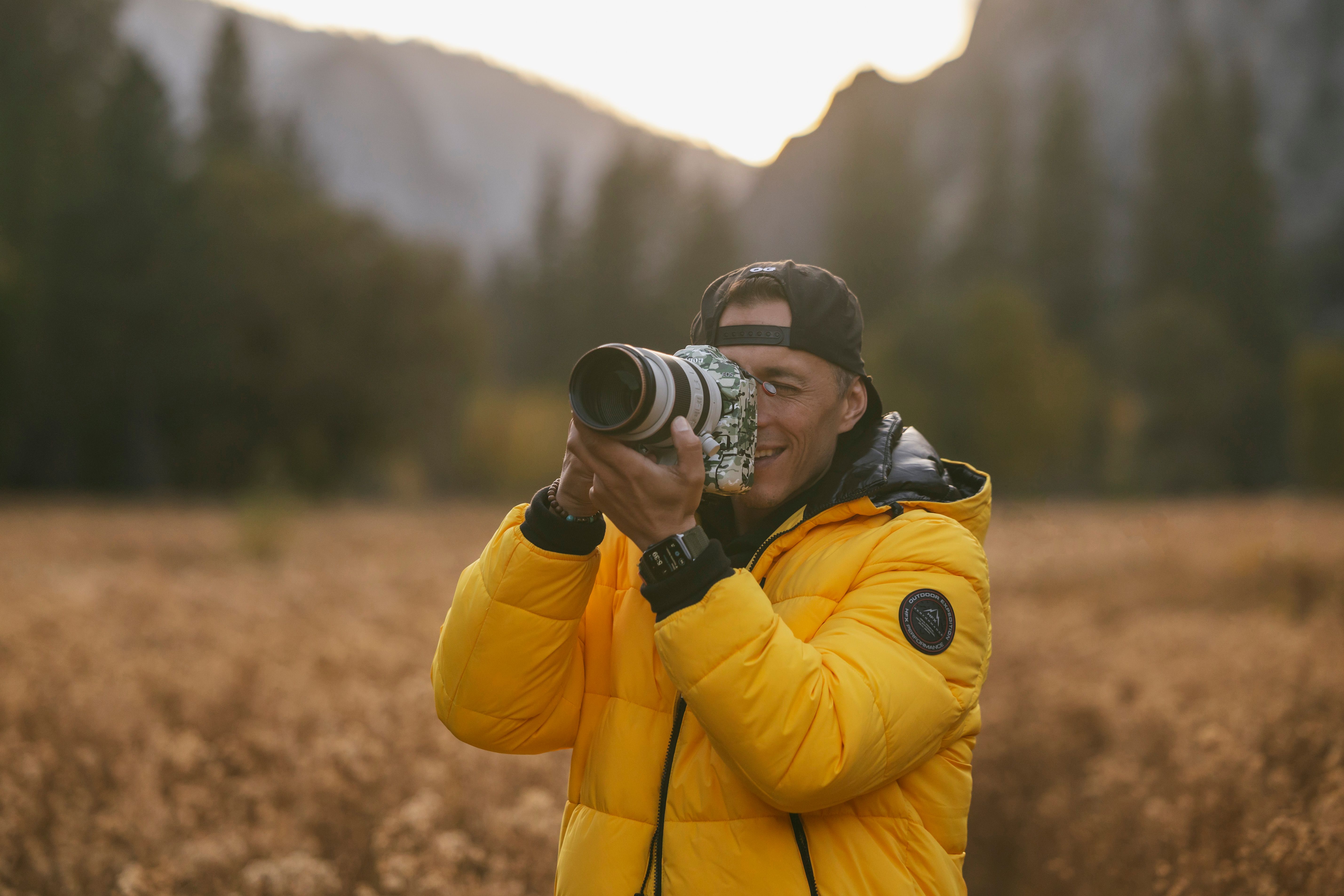 Photographer in a yellow jacket taking pictures in a scenic outdoor setting with a long lens.