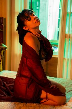 Sensual woman in lingerie posing elegantly on a bed in ambient lighting.