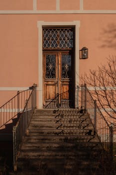 A charming vintage doorway framed by soft pink walls and casting intricate shadows in natural daylight.