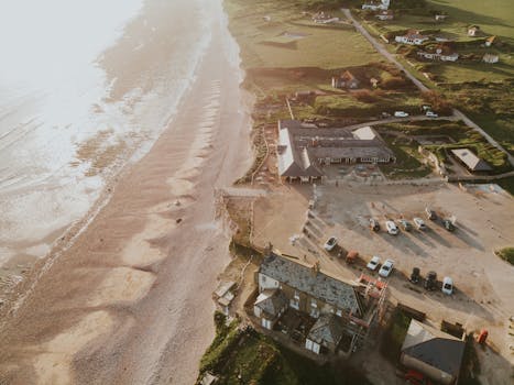 A stunning aerial view of a coastal village with a sunlit beach and parked cars at sunset.